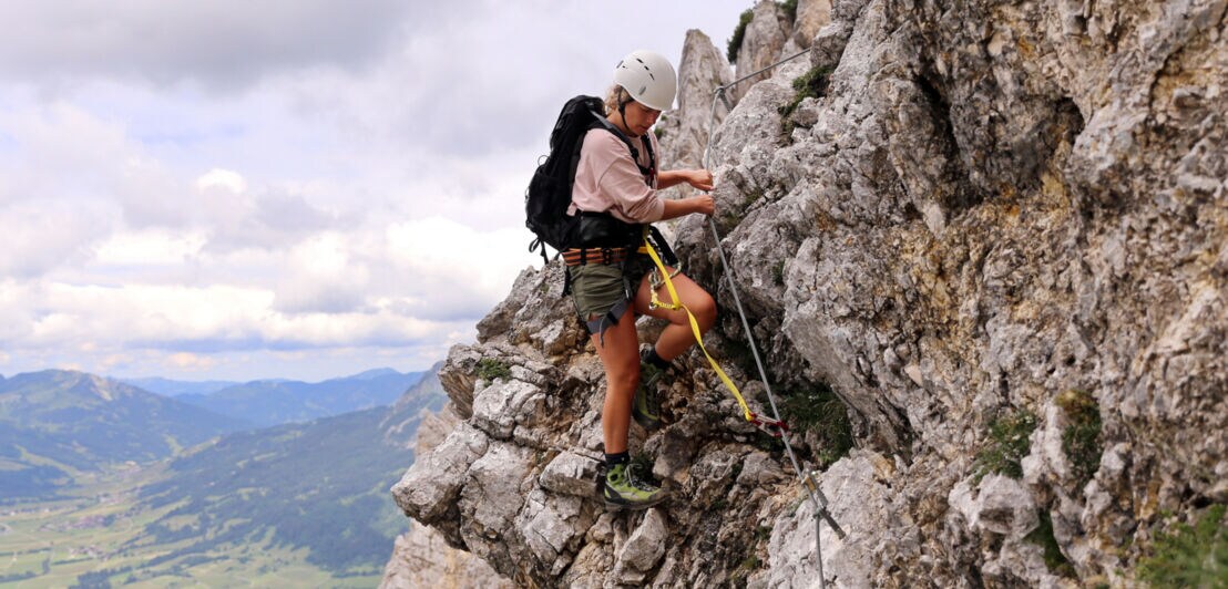 Eine junge Frau klettert am Friedberger Klettersteig am Seil entlang