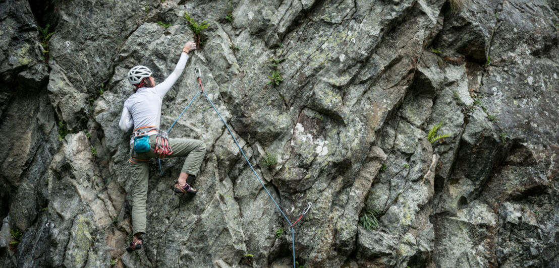 Eine junge Frau mit Helm klettert mit einem Seil an einer Felswand empor