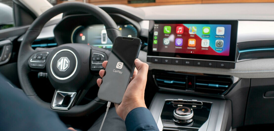 Innenraum eines Fahrzeugs mit großem Display, Fahrer vorm Lenkrad hält ein Handy in der Hand