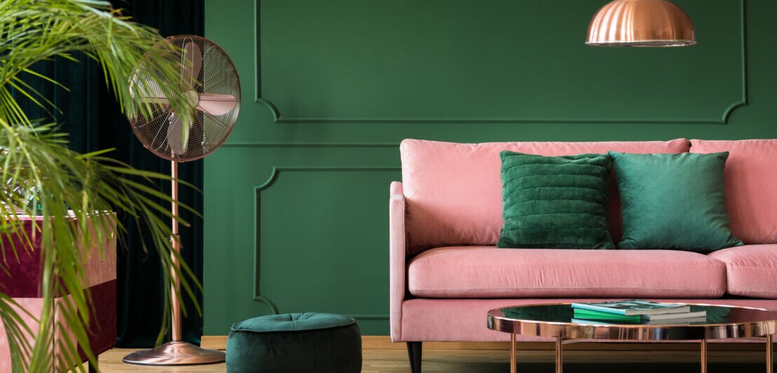 Ein modernes Wohnzimmer mit einem rosafarbenen Sofa mit grünen Kissen vor einer grünen Wand