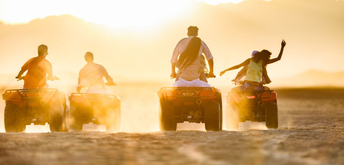 Eine Gruppe Menschen fährt auf Quads über den Sand bei Sonnenuntergang