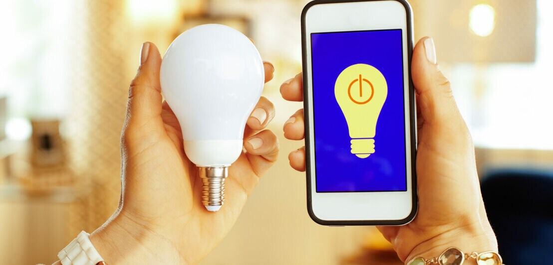 Smartphone mit Smarthome-App und smarter Glühbirne in Händen