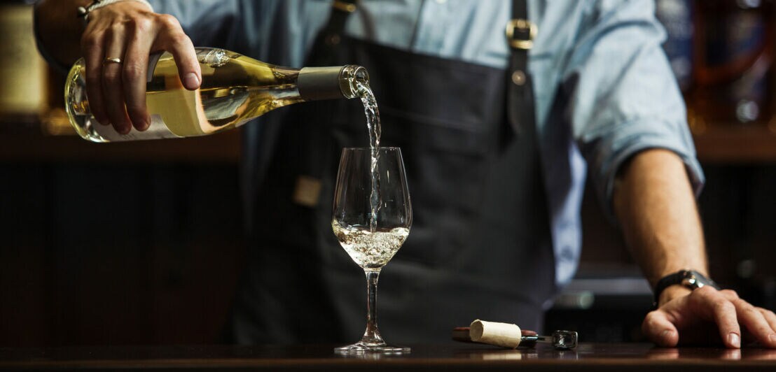 Ein Mann schenkt einen Weißwein in ein Weißweinglas ein.