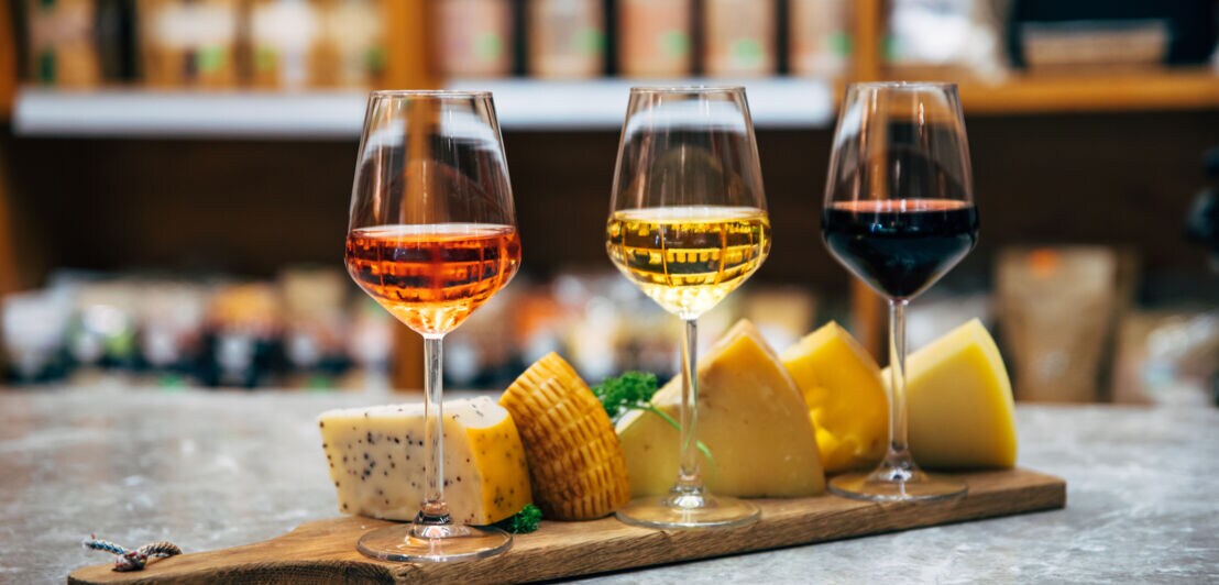 Drei Gläser mit Wein stehen auf einem Holztablett mit Käse.