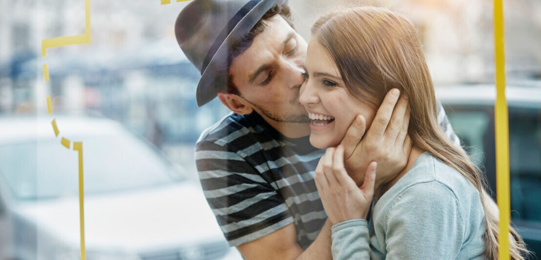 Ein junges Paar steht auf der Straße vor dem Fenster eines Cafés und umarmt sich glücklich