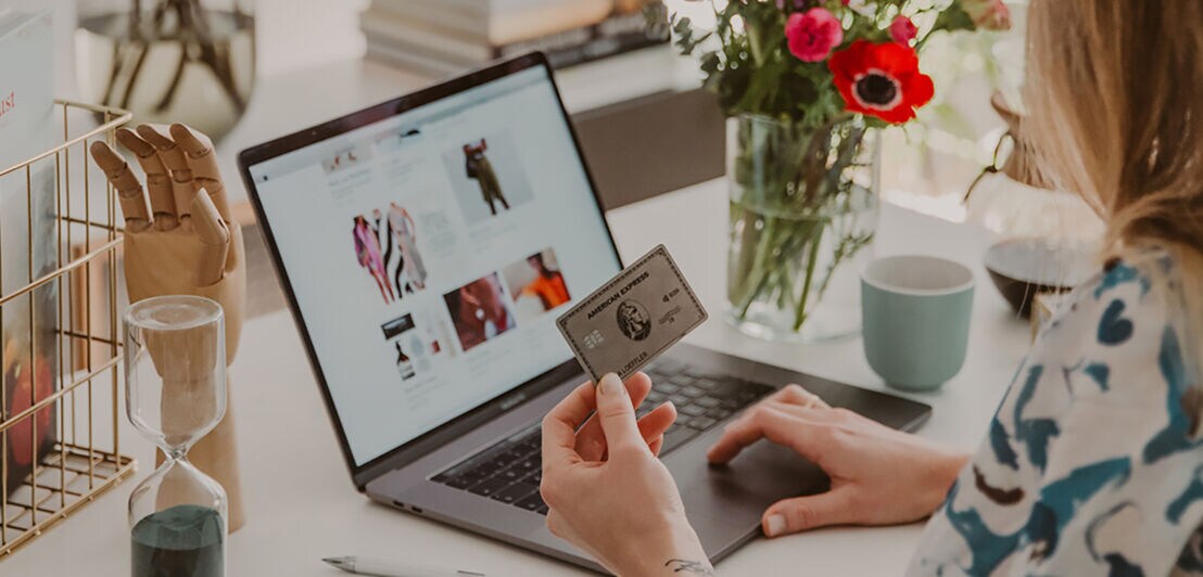 Eine Frau am Schreibtisch hält eine Amex Platinum Kreditkarte beim Online-Shopping in der Hand