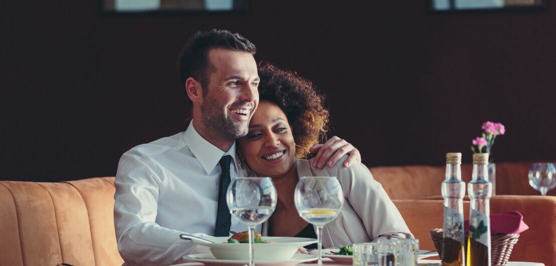 Ein glückliches Paar sitzt aneinander gekuschelt an einem gedeckten Tisch in einem eleganten Restaurant