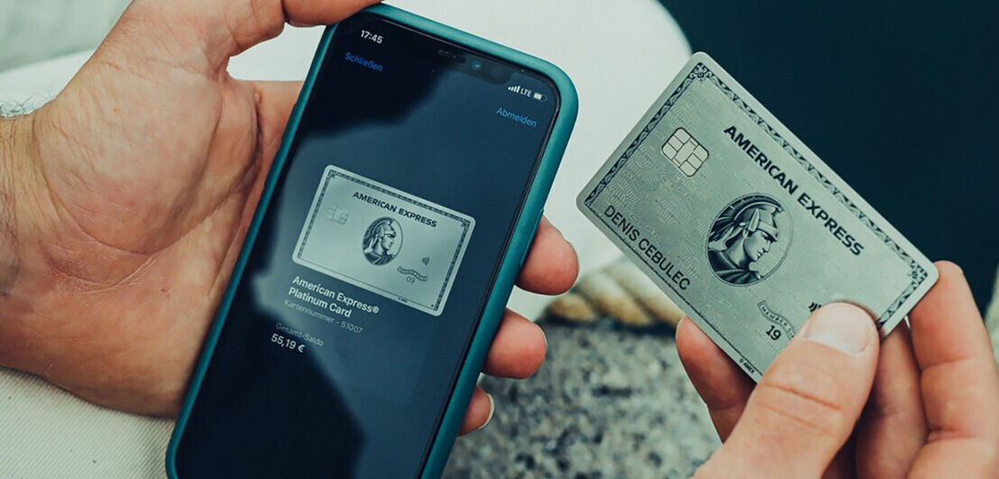 Eine Hand hält eine Amex Platinum Card neben einem Smartphone mit der Amex App