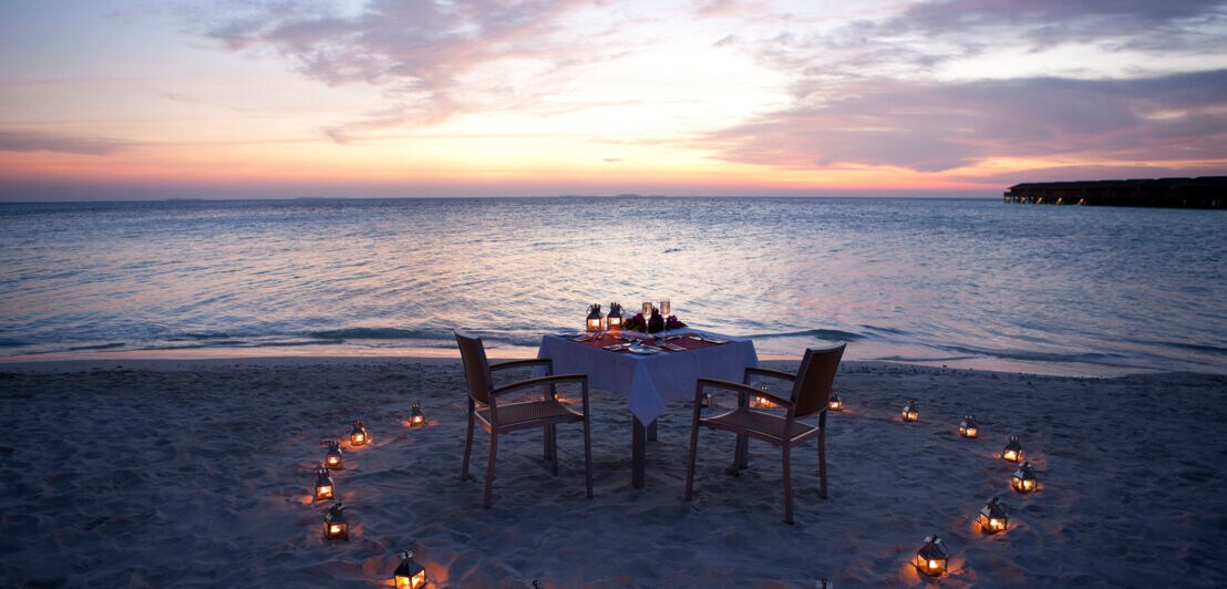 Ein romantisch gedeckter Tisch für zwei bei Sonnenuntergang am Strand 
