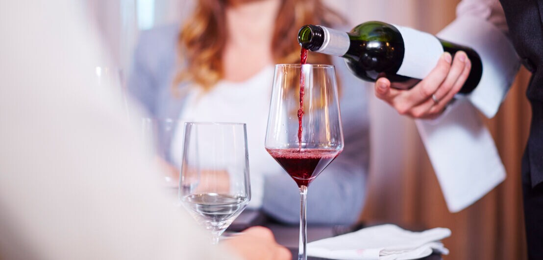 Ein Kellner gießt Rotwein in ein Glas an einem elegant gedeckten Tisch mit zwei Personen