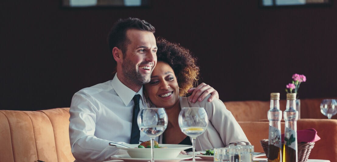 Ein glückliches Paar sitzt Arm in Arm an einem gedeckten Tisch in einem eleganten Restaurant