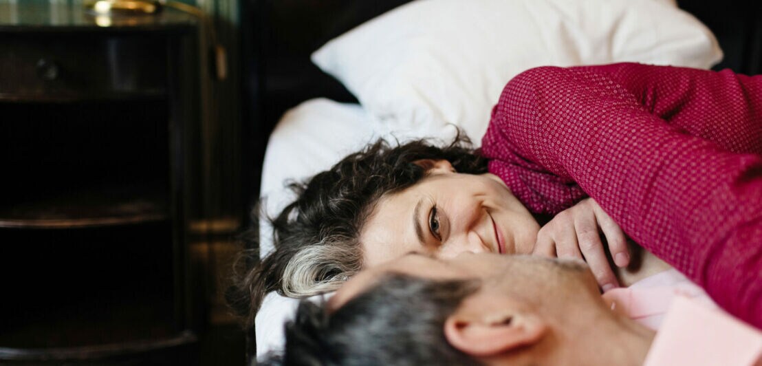 Nahaufnahme von den Köpfen eines Paares, das in einem Hotelbett liegt und sich zufrieden lächelnd anschaut