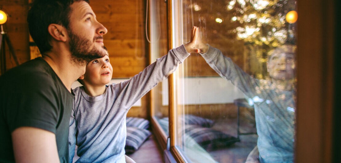Ein Mann mit Kind auf dem Schoß blickt aus dem Fenster