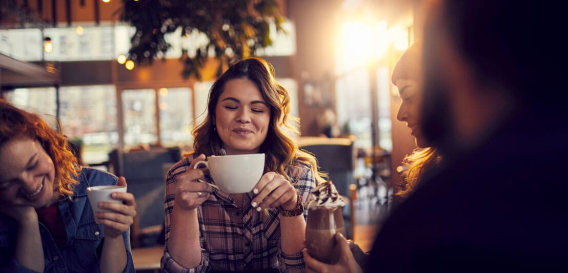 Eine junge Frau genießt eine Tasse Kaffee in Gesellschaft ihrer Freunde in einem Café