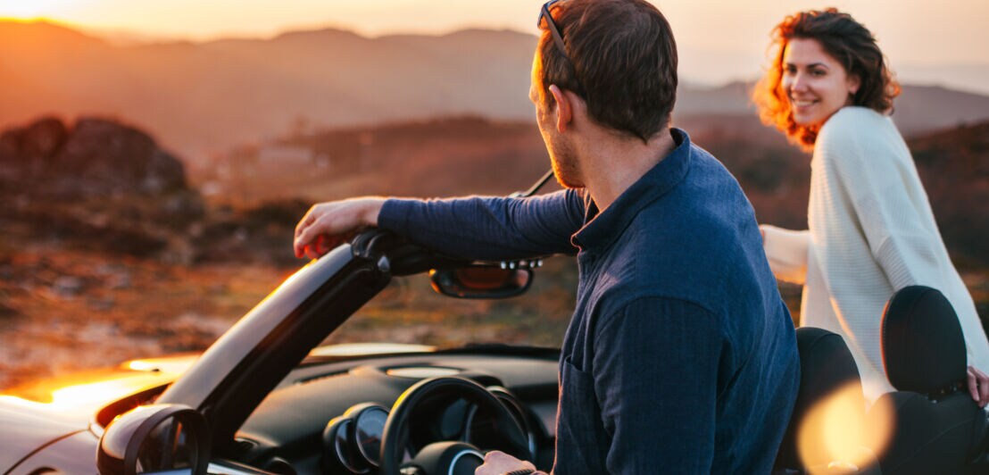 Rückansicht eines Paares, das aus einem Cabriolet in eine Wüstenlandschaft bei Sonnenuntergang schaut