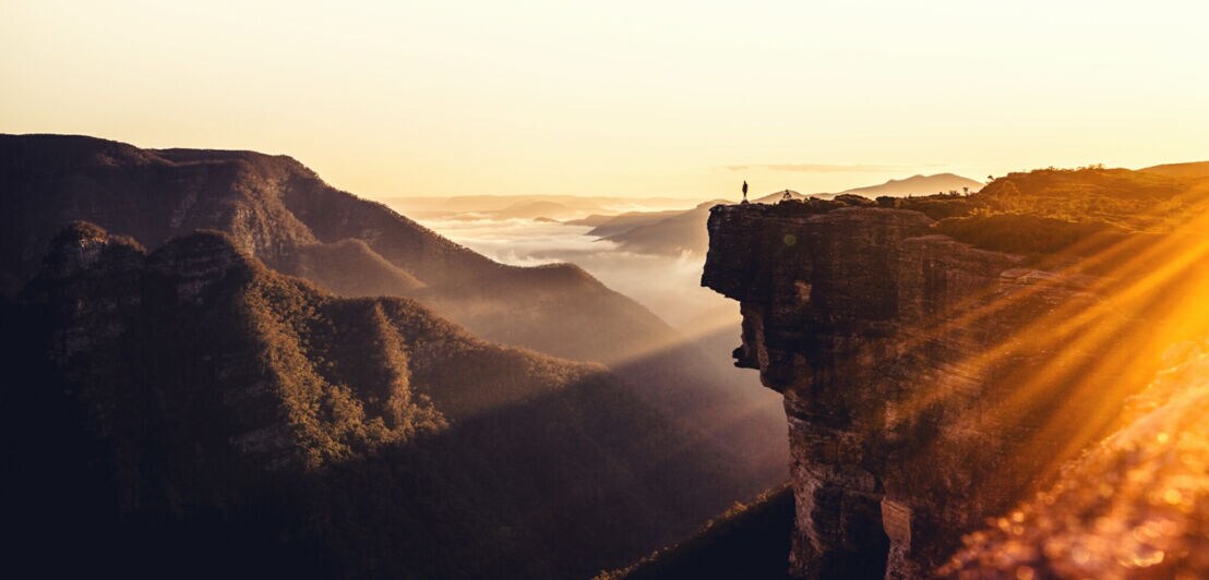 Panoramasicht einer gebirgigen Landschaft mit einer Person am Rande einer Klippe bei Sonnenaufgang