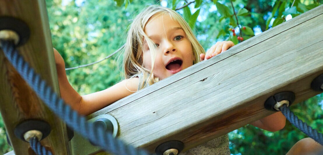 Ein kleines Mädchen klettert auf einem Klettergerüst