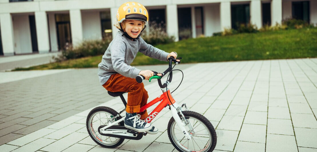 Ein kleiner Junge fährt auf seinem Fahrrad vor einem Wohnhaus