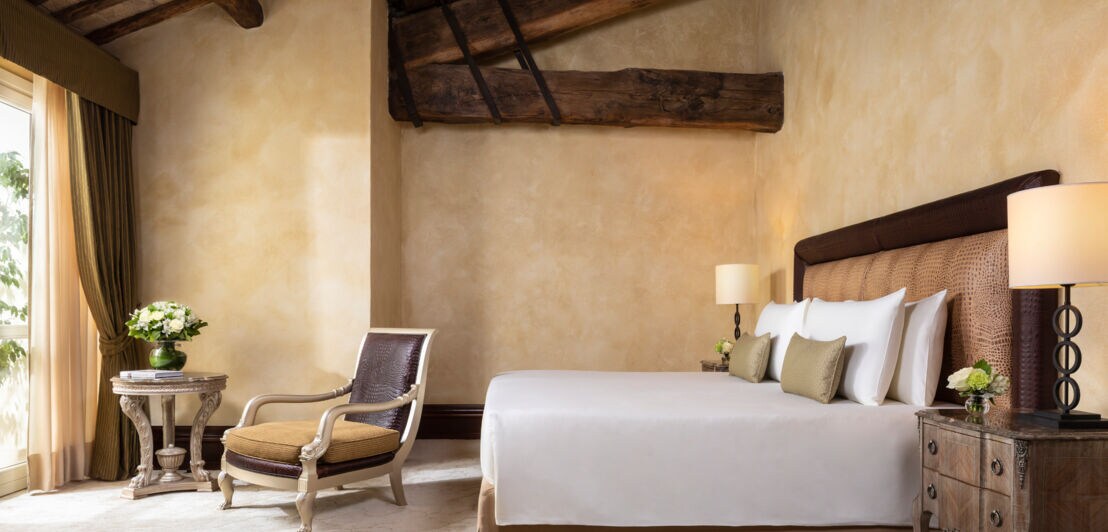 Innenausstattung eines stilvoll eingerichteten Hotelzimmers mit Doppelbett und massiven Deckenbalken aus Holz