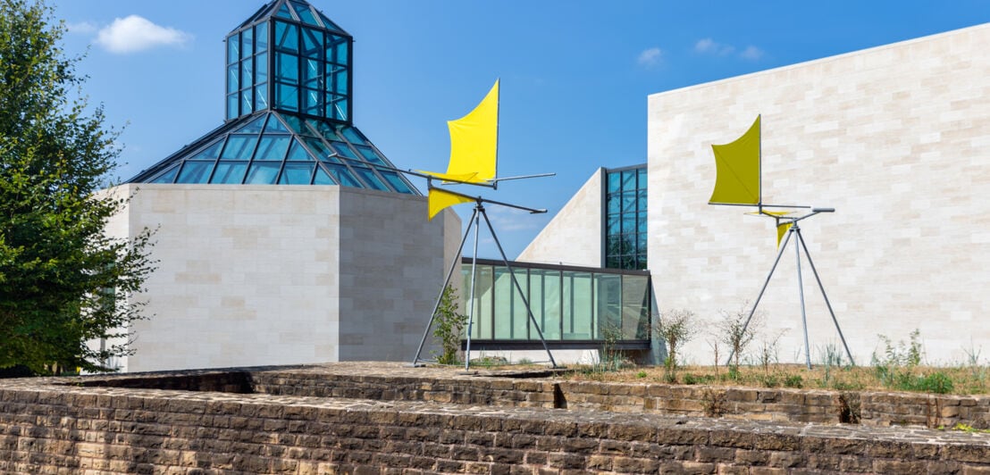 Ein modernes Gebäude vor dem eine gelbe Kunst-Installation steht.
