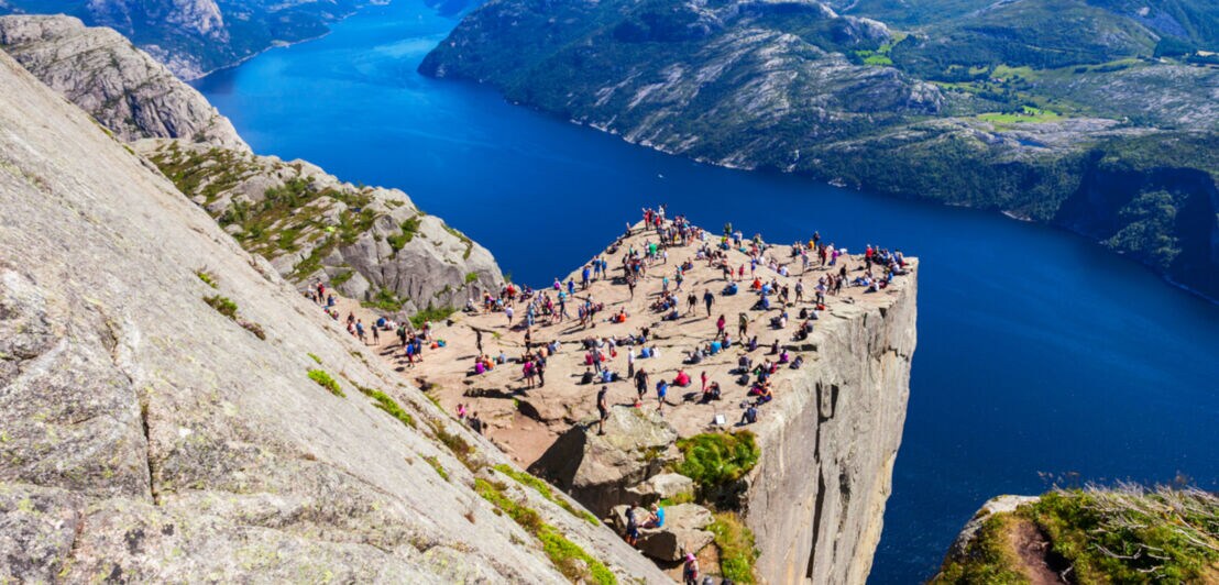 Ein Felsvorsprung mit vielen Menschen an einem Fjord