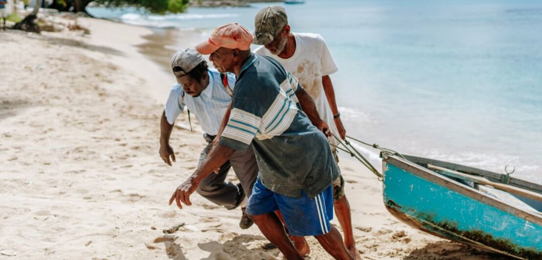 Drei Männer ziehen per Hand ein kleines Boot an den Strand.