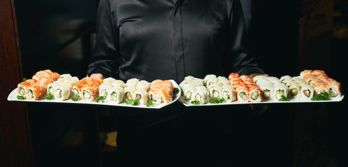 Eine Frau trägt zwei Platten mit Sushi.