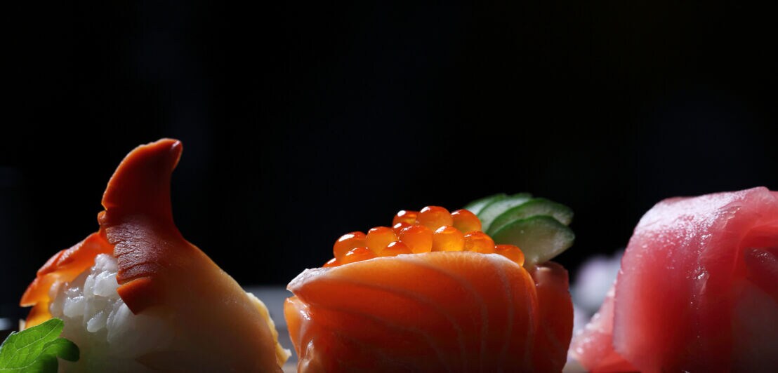 Drei verschiedene Sushi vor einem schwarzen Hintergrund.
