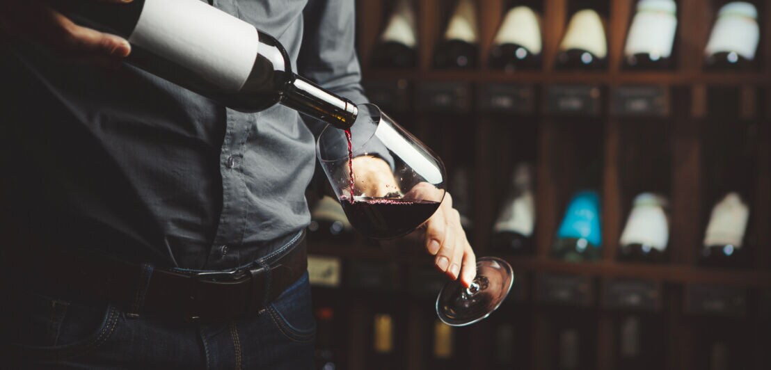 Ein Mann schenkt Rotwein in ein Glas ein