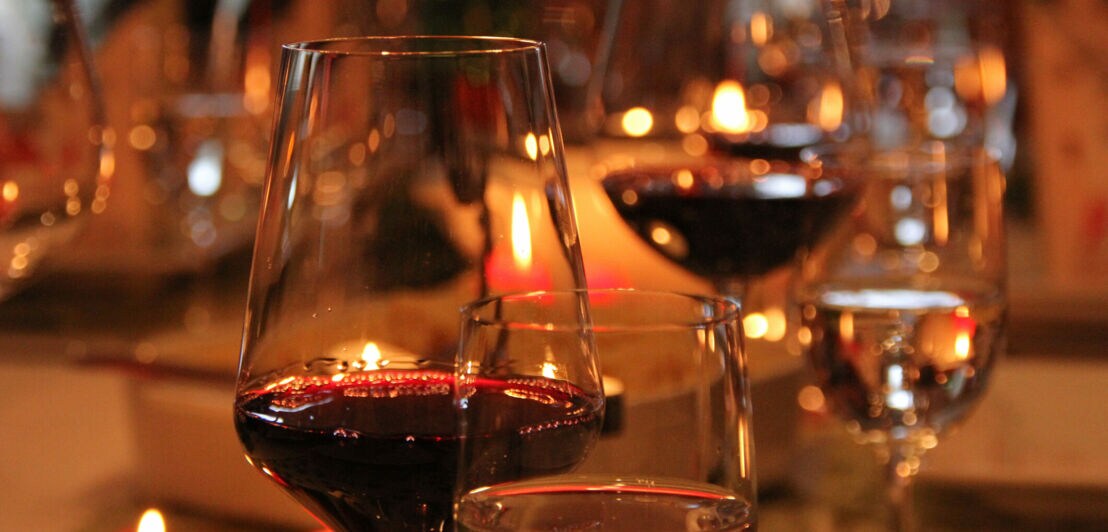 Rotwein in Weingläsern auf einem Tisch, im Hintergrund Kerzen