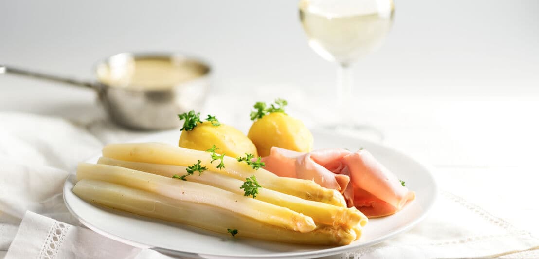 Ein Teller mit Spargel, Kartoffeln und Schinken mit einem Glas Wein