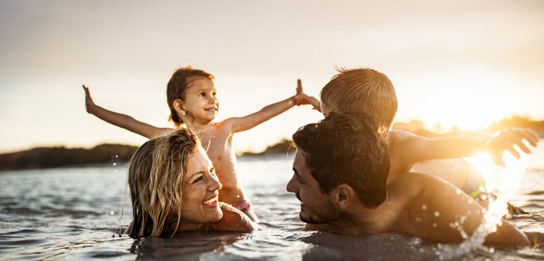 Eine junge, glückliche Familie mit zwei Kindern badet im Meer bei Sonnenuntergang