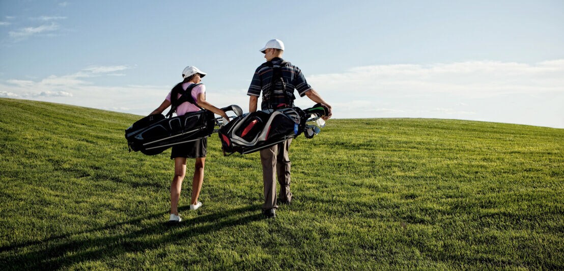 Ein Pärchen trägt sein Golfequipment über einen Golfplatz