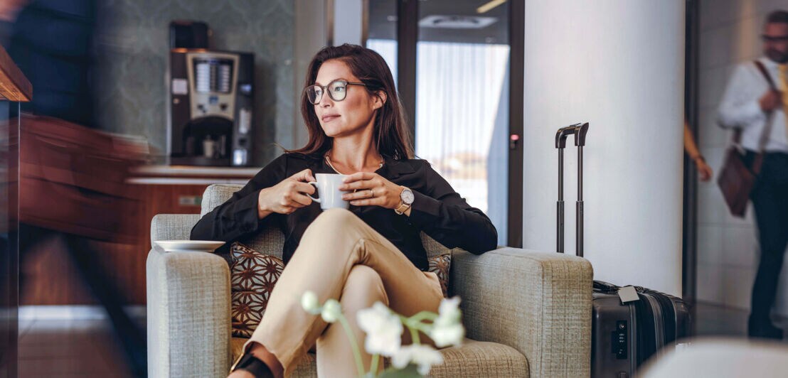 Eine Geschäftsfrau wartet entspannt mit einer Tasse Kaffee in der Flughafen-Lounge