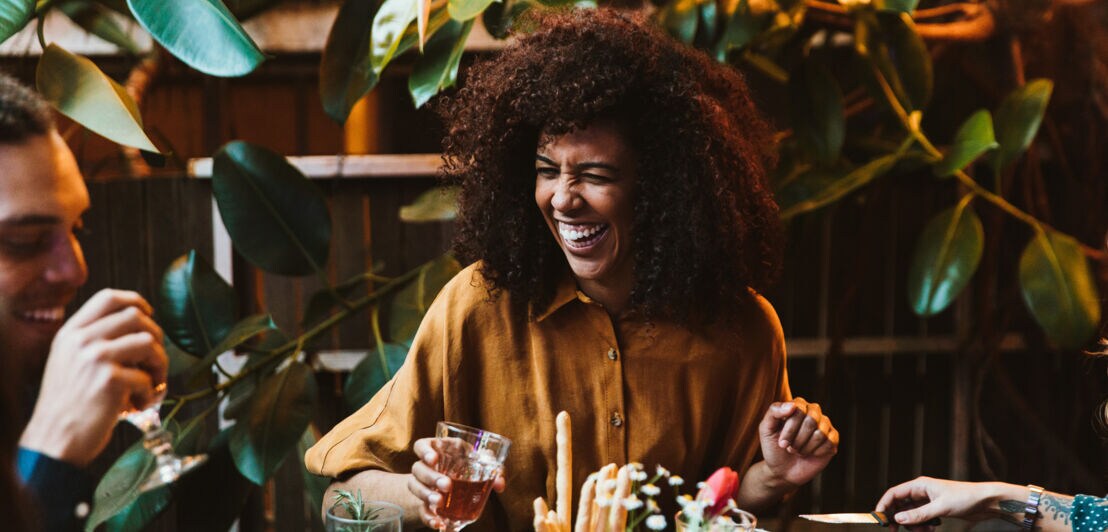 Eine lachende Frau an einem Restauranttisch in Gesellschaft von Freunden