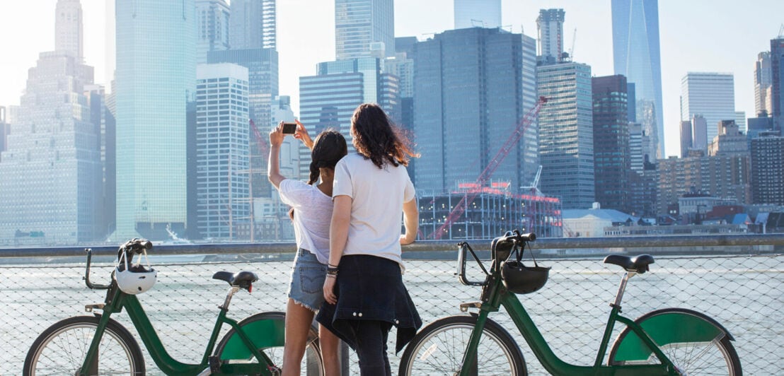 Rückansicht eines jungen, coolen Paares mit Fahrrädern, das auf die Skyline von Manhattan blickt
