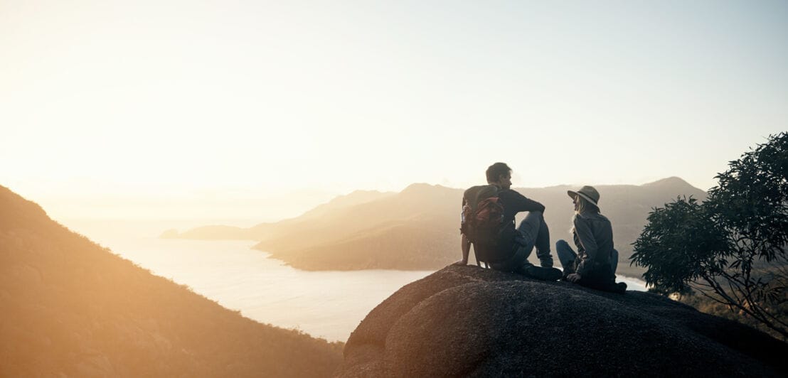 Ein Paar sitzt auf einem Felsvorsprung über einer Bucht im Sonnenuntergang