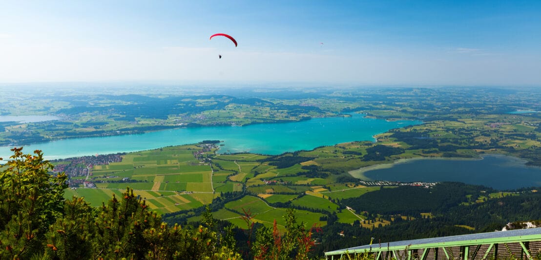 Ein Paraglider fliegt über eine Landschaft, bestehend aus Feldern und Seen.