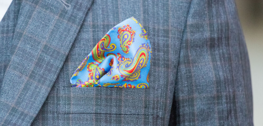 Nahaufnahme eines bunten Einstecktuchs mit einem modernen Paisley-Muster auf einem karierten Anzug