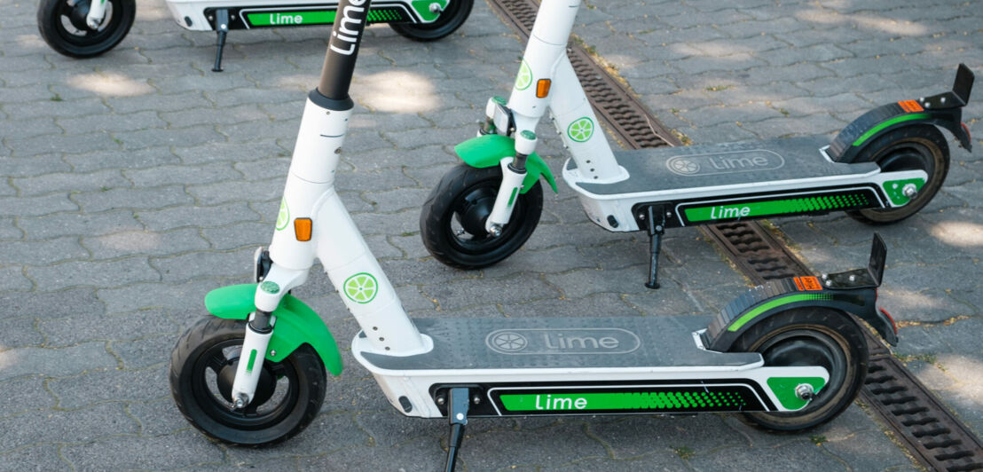 Vier grüne E-Scooter stehen geparkt auf der Straße