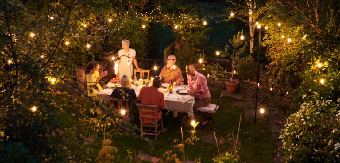 Eine Gruppe Freunde sitzen beim Abendessen in einem stimmungsvoll beleuchteten Garten