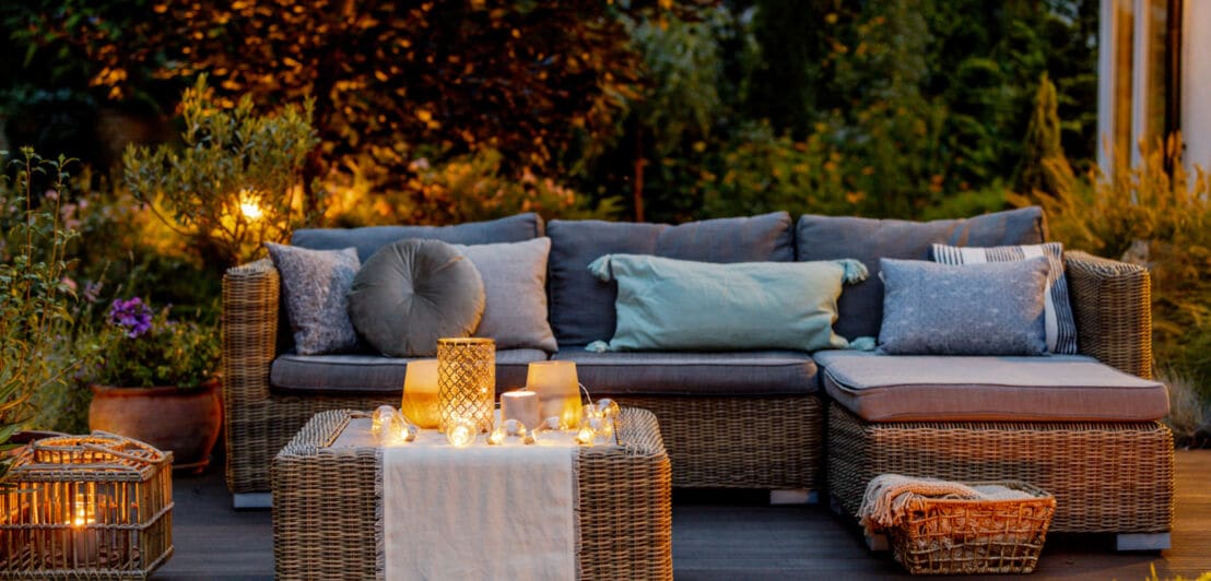 Ein Sofa auf einer Terrasse, dekoriert mit brennenden Kerzen und Windlichtern in der Abenddämmerung