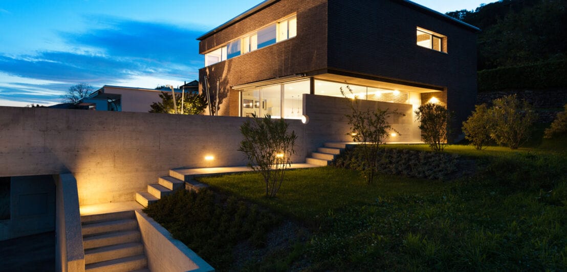 Ein modernes Haus mit beleuchtetem Treppenaufgang und Garten in der Abenddämmerung