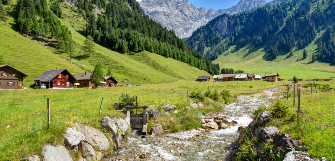 Holzhütten am Fuße der Alpen mit einem Bachlauf davor