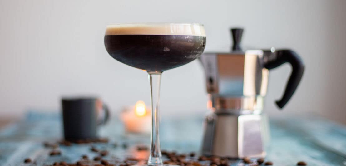 Ein Cocktail mit Kaffee zubereitet in einem Martiniglas, daneben eine Kaffeekanne