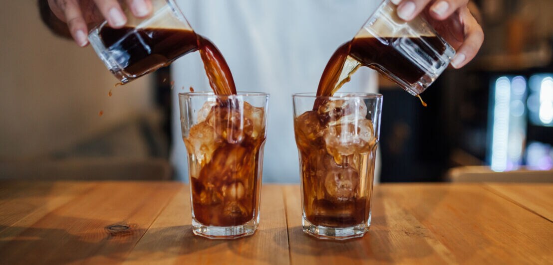 Ein Barista gießt Kaffee in zwei Gläser voller Eiswürfel