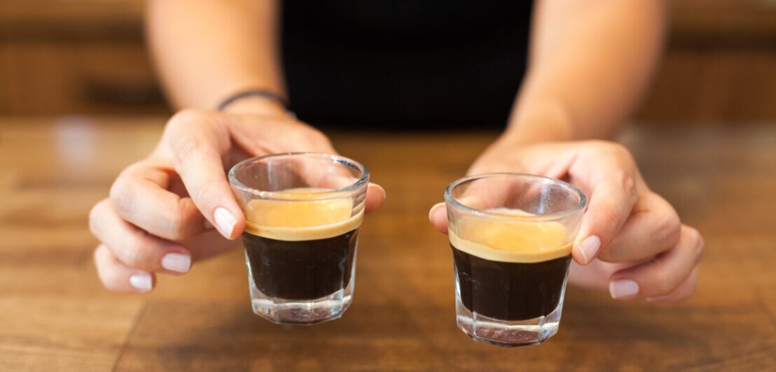 Eine Frau hält zwei Gläser mit Espresso in den Händen