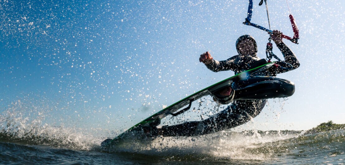 Kitesurfer macht einen beeindruckenden Darkslide-Trick mit viel Sprühwasser