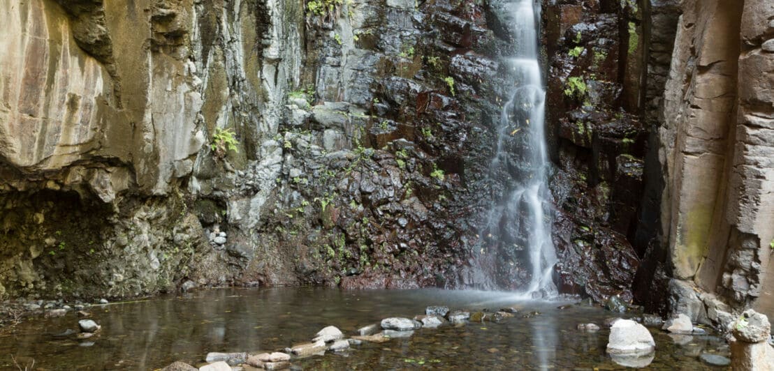 Ein kleinerer Wasserfall, der zwischen Felswänden herabfällt und in einem kleinen Teich endet