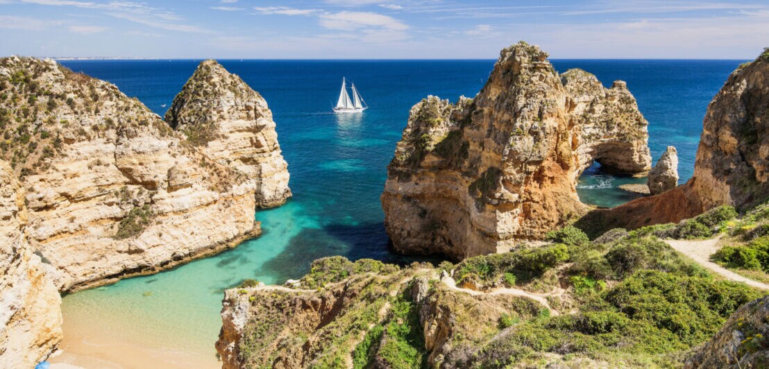 Eine kleine Bucht an der Algarve mit Felsformationen und einem Segelboot im türkisblauen Meer